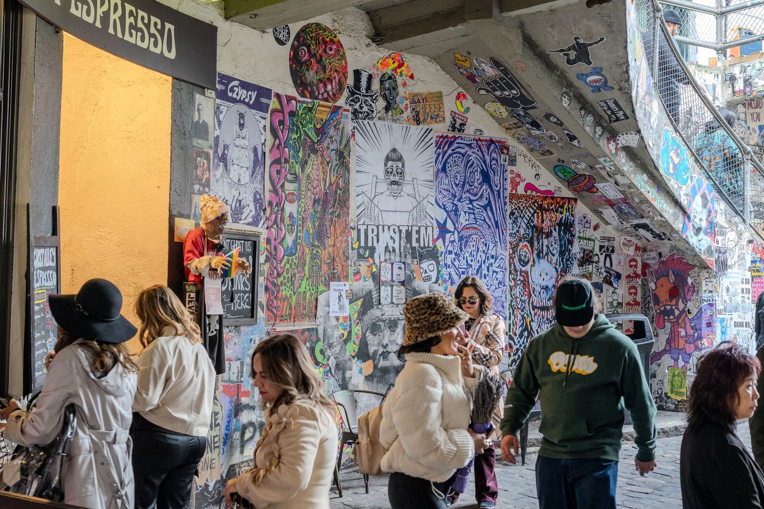 People walking past vibrant graffiti-covered walls in an urban alley near an espresso shop.