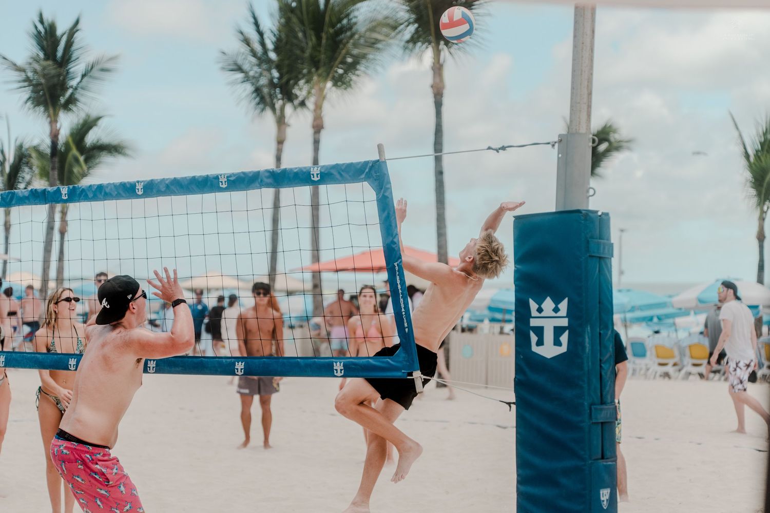 Beach volleyball player jumping to spike the ball at the net on a sunny tropical beach resort.