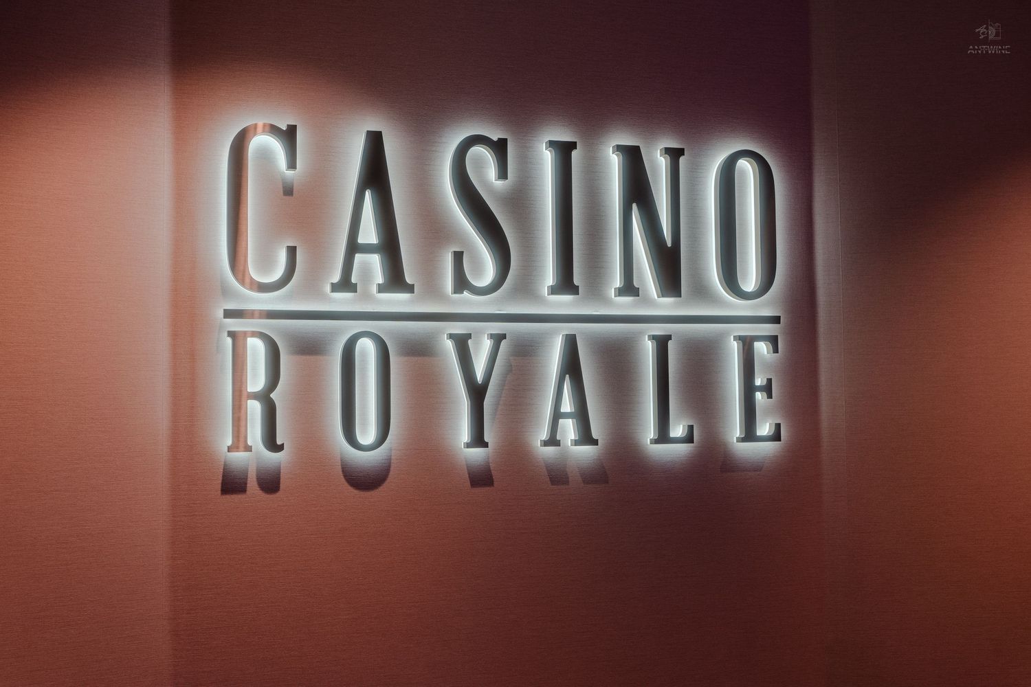 Illuminated Casino Royale sign with backlit letters on a warm-toned wall inside a cruise ship.