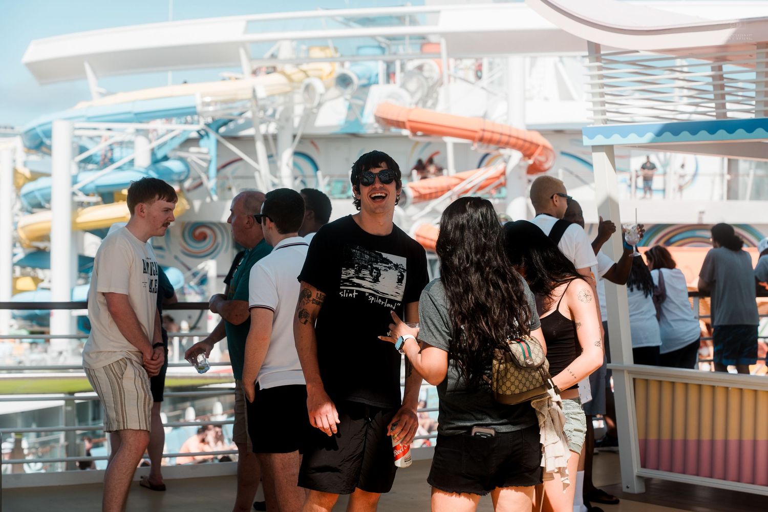 Group of passengers in black outfits socializing on a cruise ship deck near a water slide.