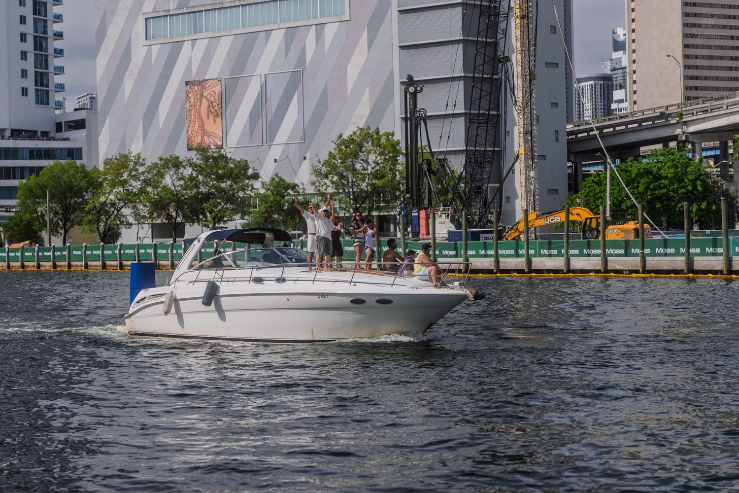 A white motorboat with passengers cruising along a city waterway with modern buildings behind.