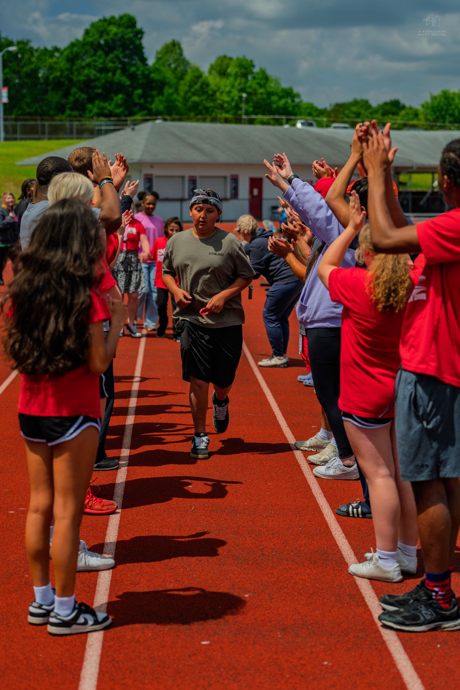 Students in red uniforms form a celebratory tunnel on a red track, high-fiving a runner during a school sports event.