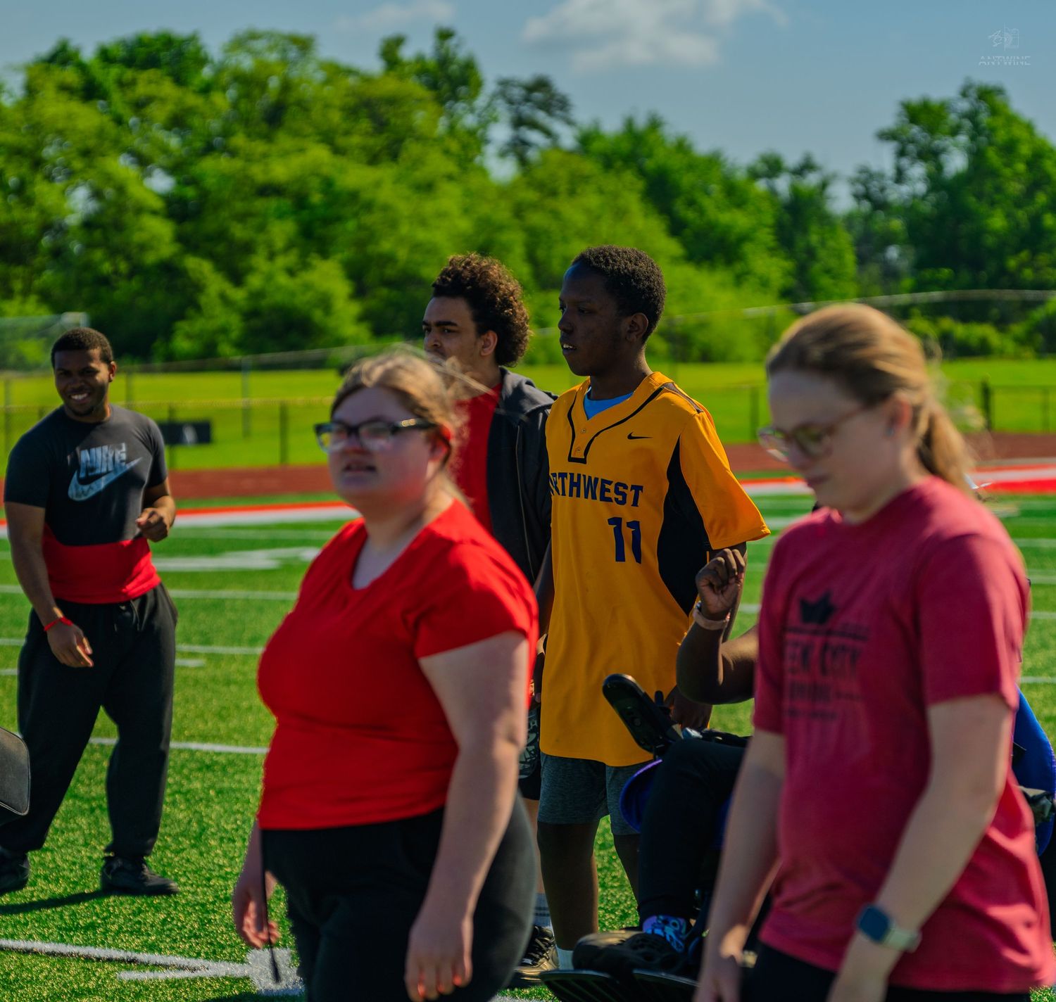 Students in athletic wear walk on a green turf sports field during an outdoor school track and field event.