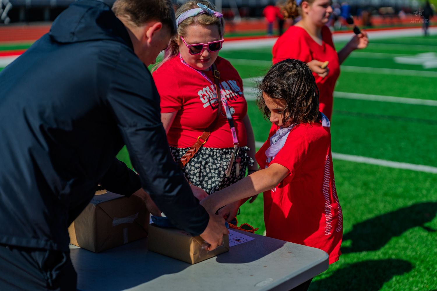 Woman and child in red Colorado shirts examining a cardboard box at an outdoor stadium event.
