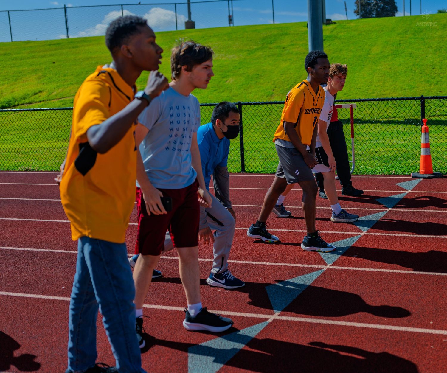 Students line up on a red running track during an outdoor athletic event on a sunny day.