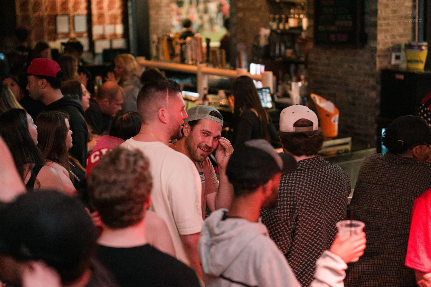 Group of people socializing and laughing near a bar counter in a crowded nightlife venue.