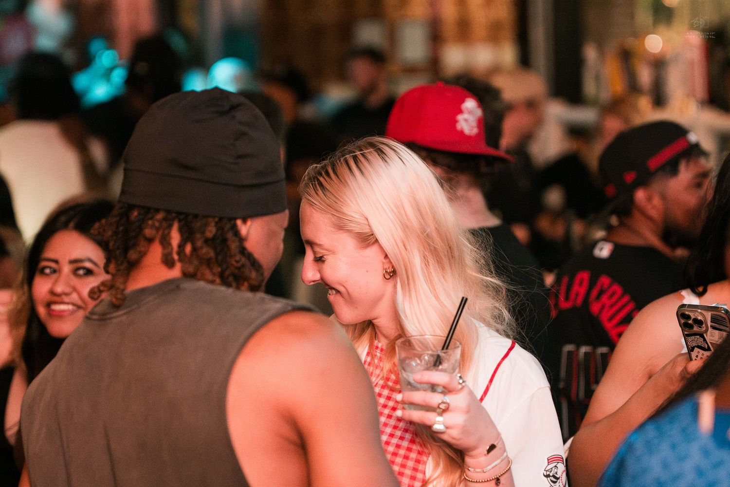 Smiling blonde woman holding a drink socializing in a busy nightclub crowd.