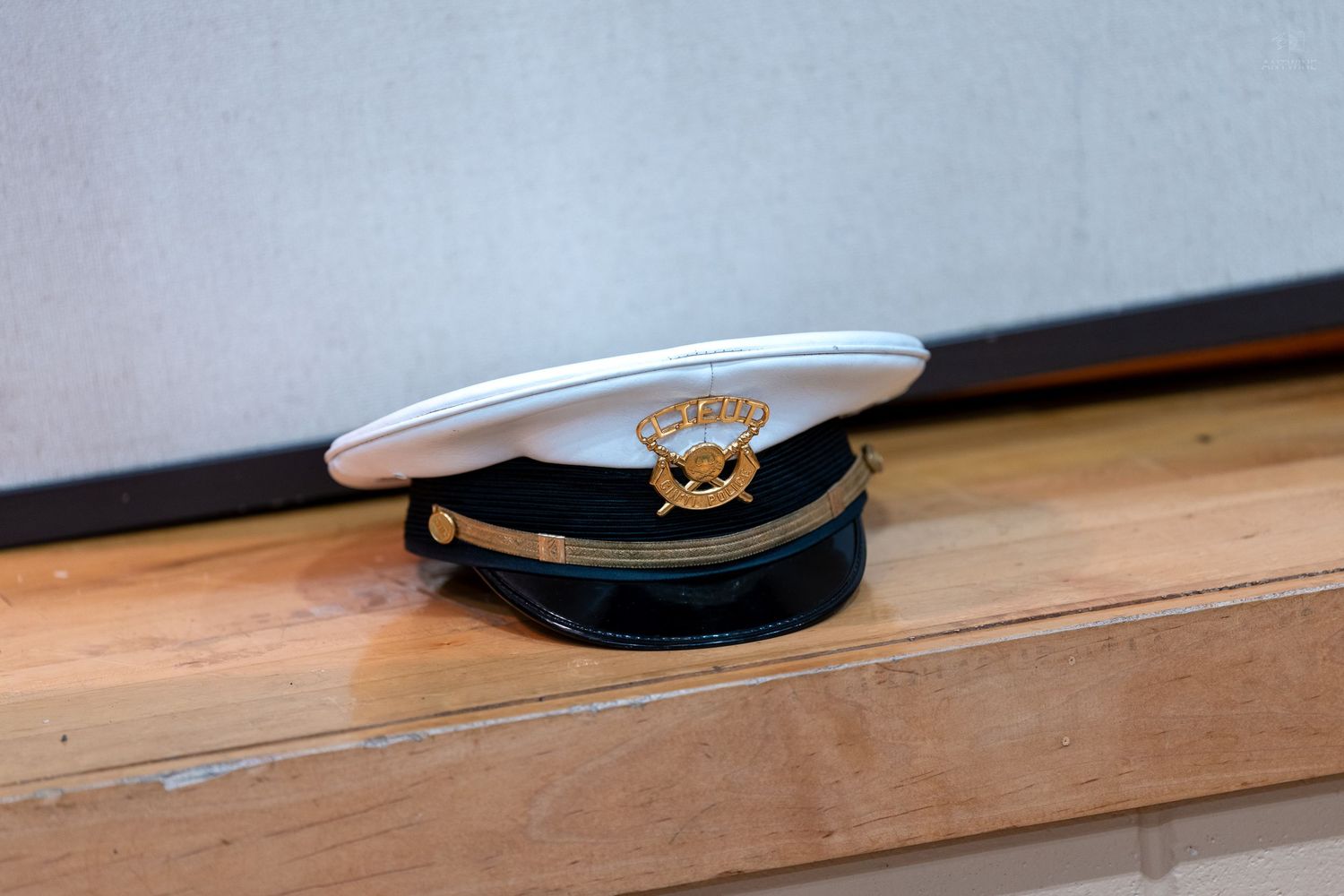 White military-style captain hat with gold emblem resting on a wooden surface indoors.