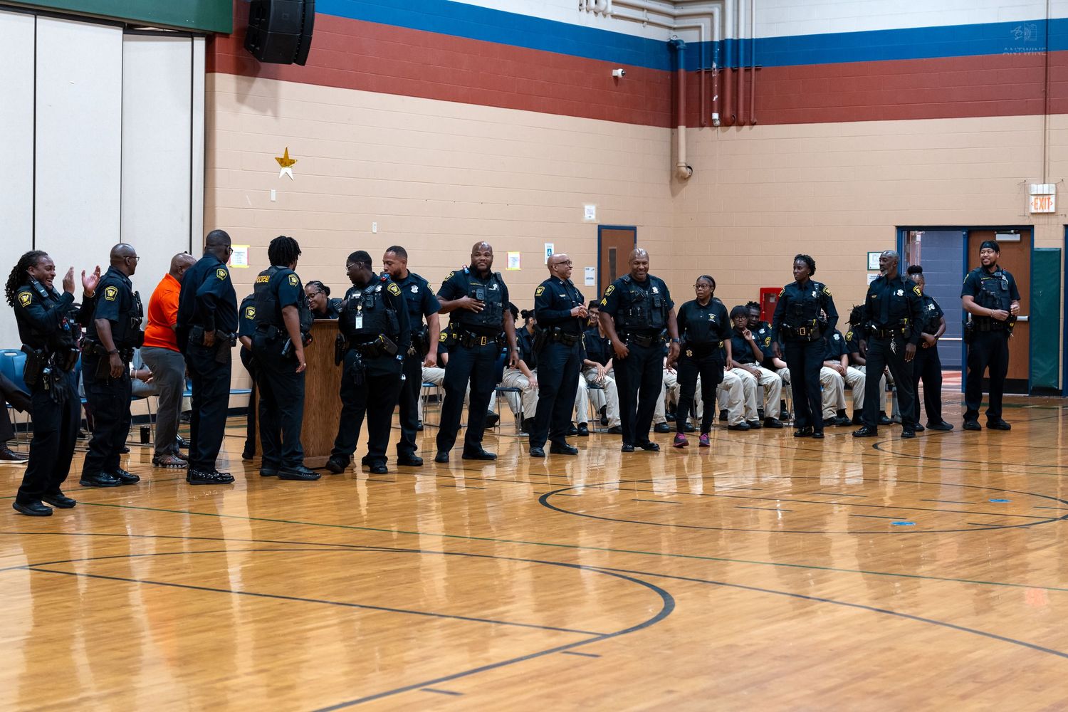 Police officers stand in a line inside a gymnasium during a community event on a hardwood basketball court.