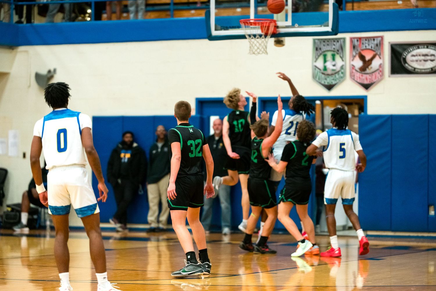 High school basketball players compete for a rebound near the basket during an indoor gym game.