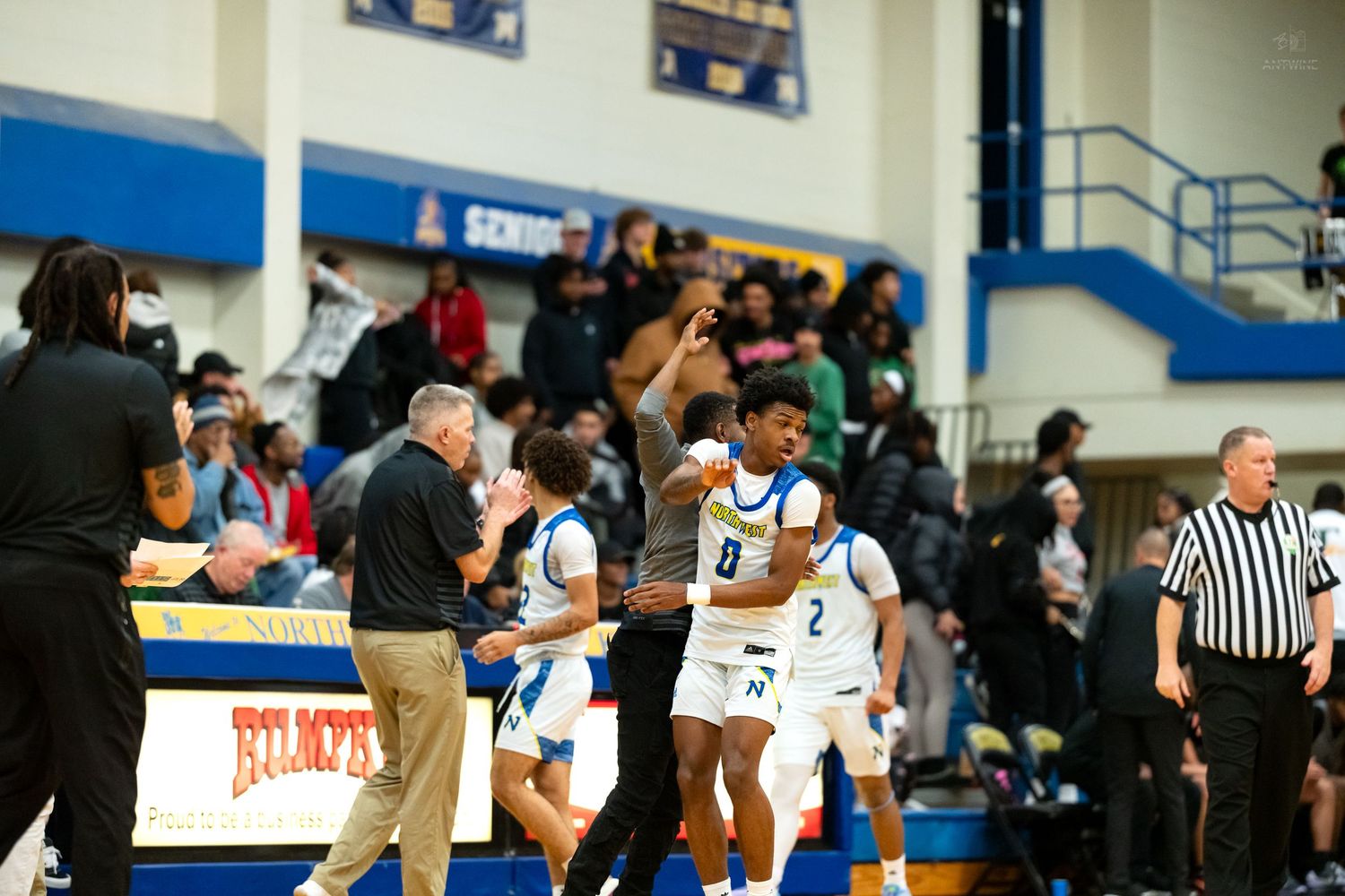 High school basketball players celebrate on the sideline during an exciting indoor gymnasium game.