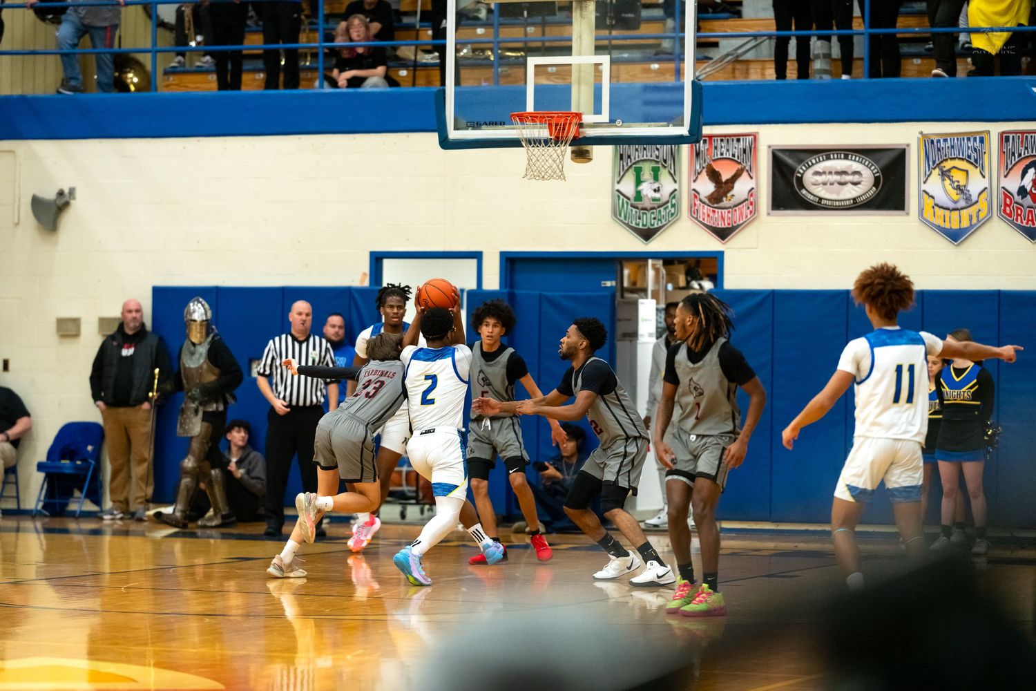 High school basketball player number 2 in white passes the ball during a competitive indoor gym game.