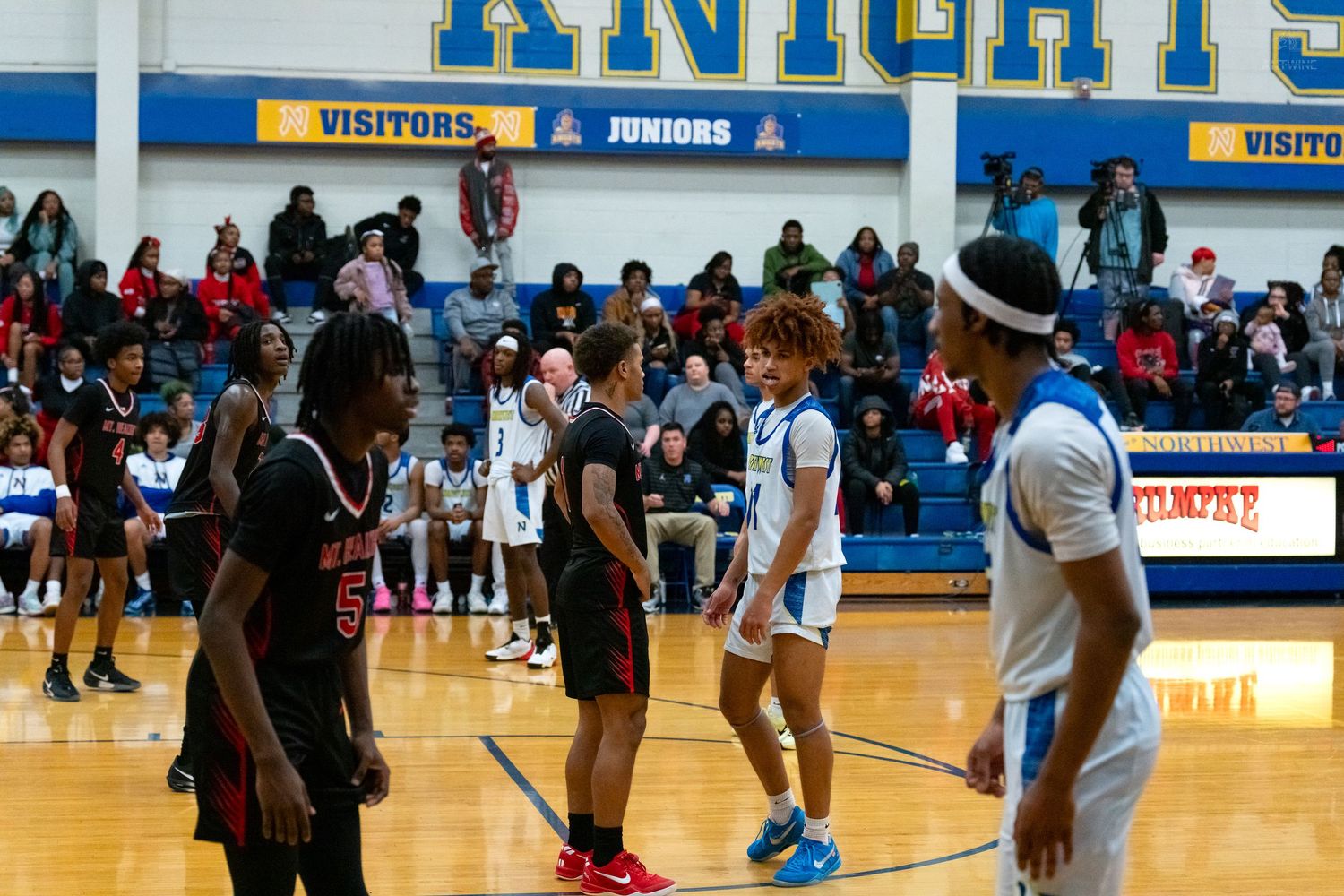 High school basketball players shake hands at center court before a game in a blue gymnasium.