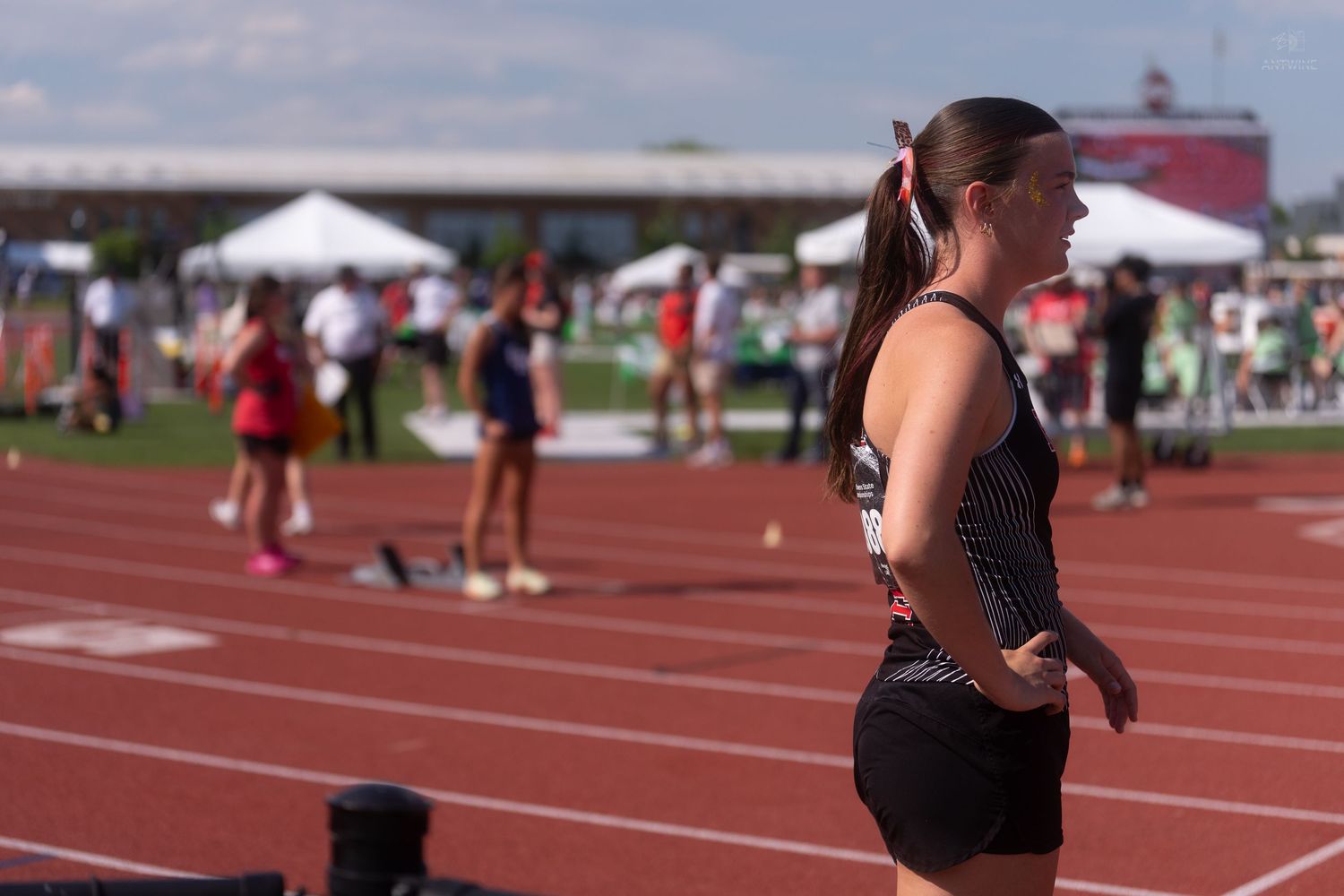Female track athlete with ponytail stands on red track during outdoor track and field competition.