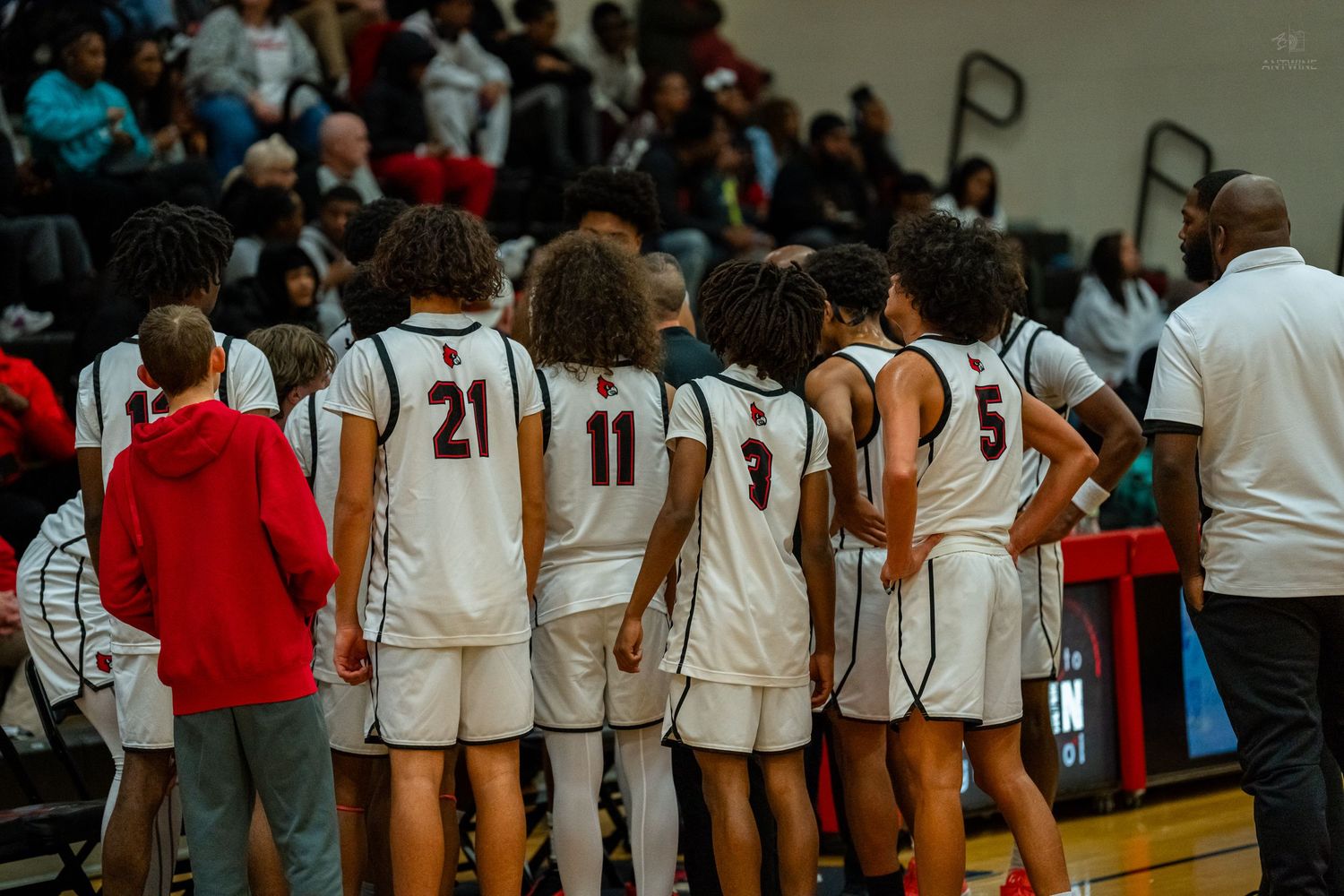High school basketball team lines up along the sideline wearing white uniforms with numbers 21, 11, 9, and 5.
