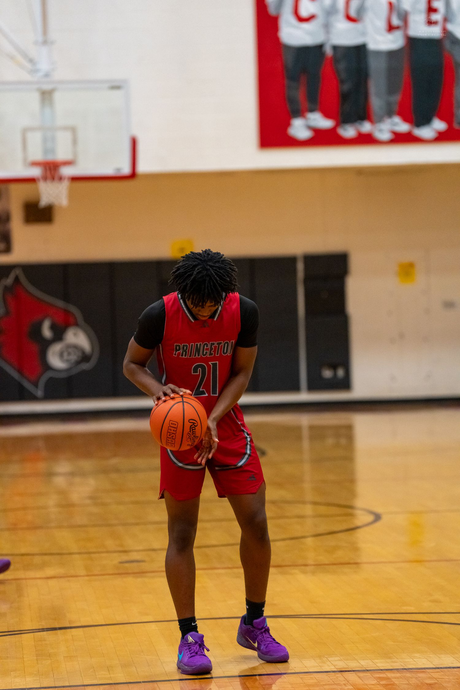 Princeton basketball player #21 dribbles ball during free throw attempt in red uniform with purple shoes.