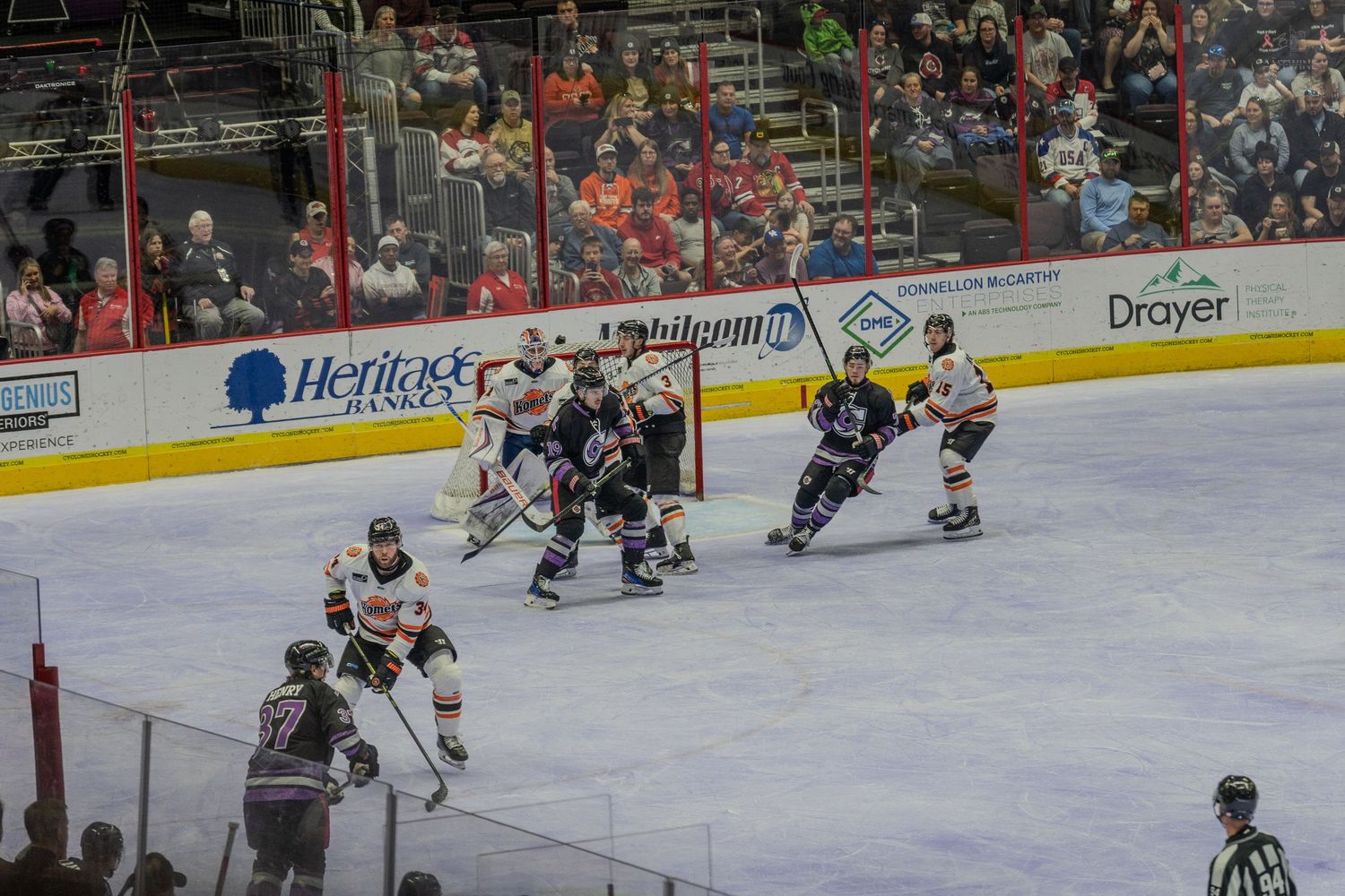 Hockey players compete near the goal crease during a fast-paced professional indoor ice hockey game.