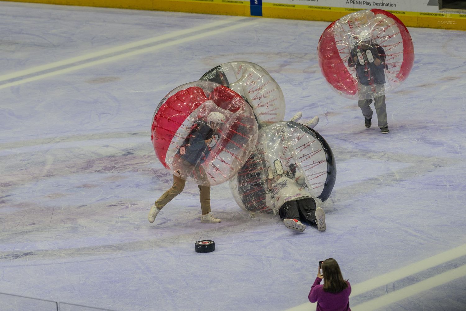 People playing bubble soccer on an ice rink, with two players colliding in large inflatable zorb balls.