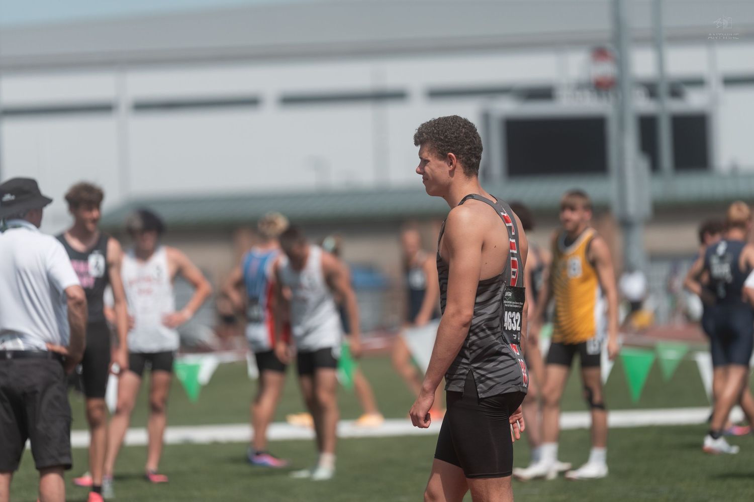 Young male track athlete wearing bib number 82 standing among competitors at an outdoor track meet.