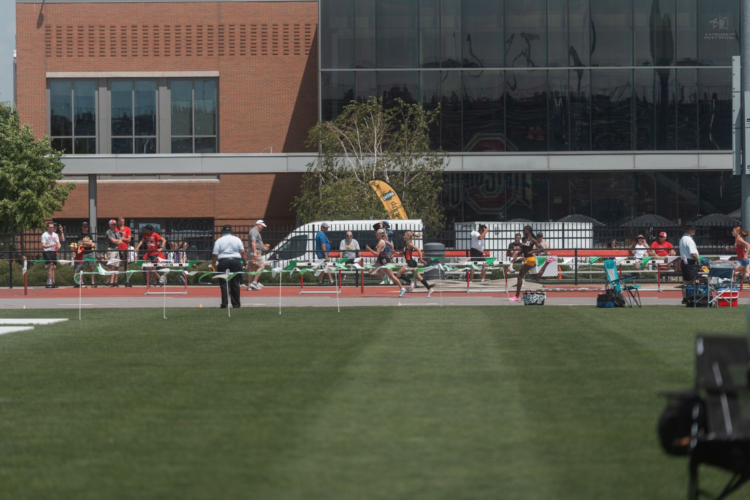 Athletes competing in track and field events on red track beside modern brick building.