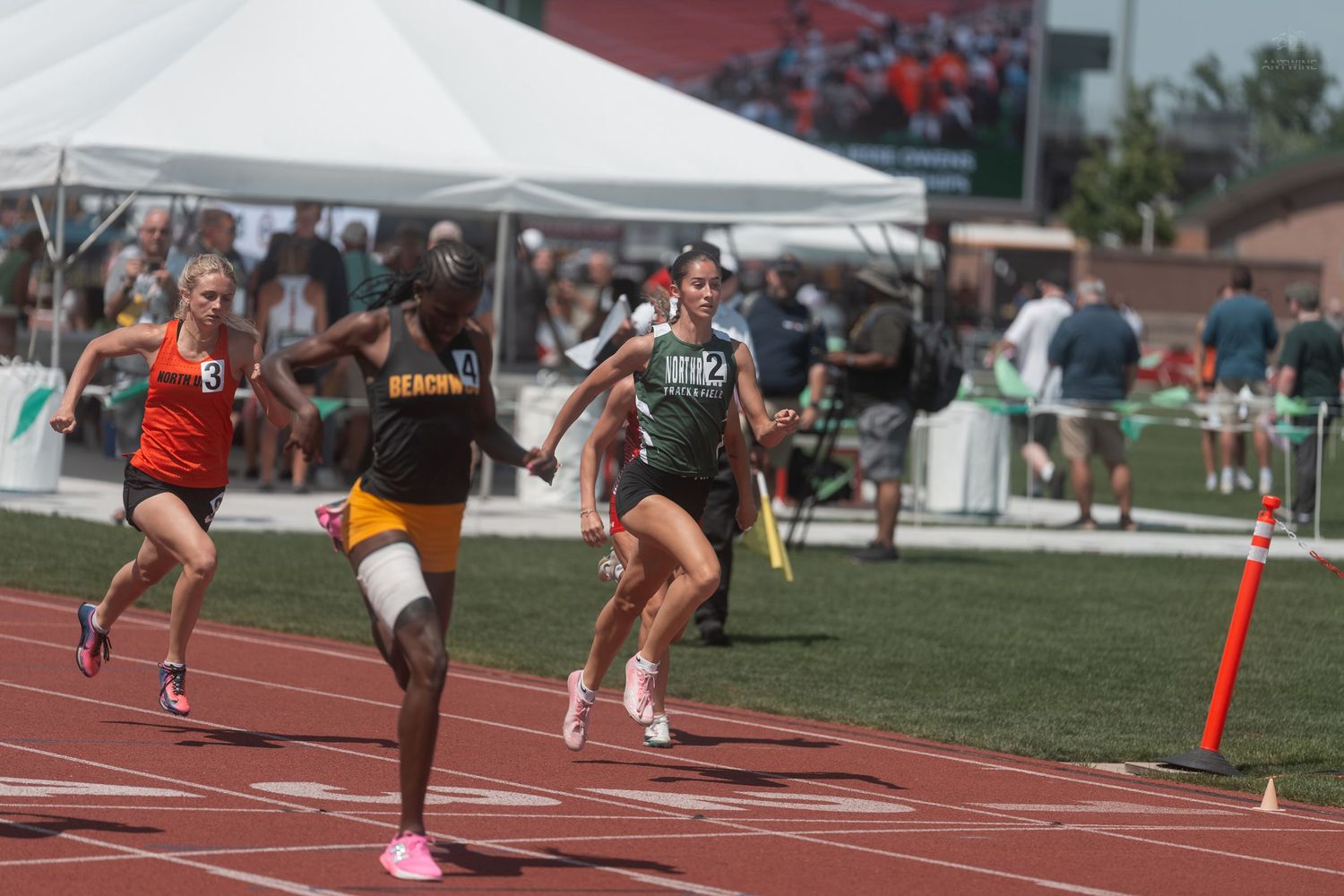 Female athletes exchange a baton during a relay race at a high school track and field competition.