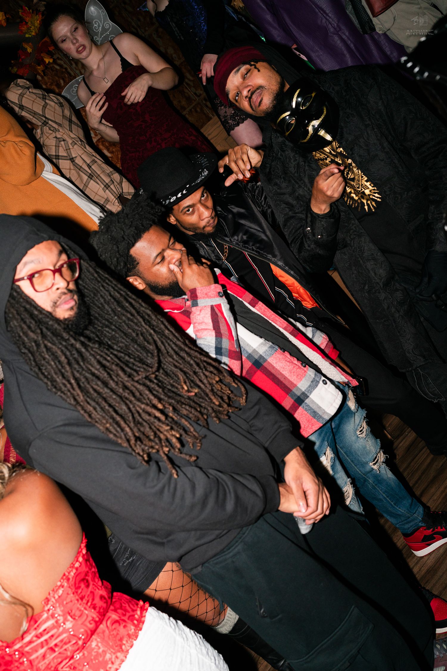 Group of friends in Halloween costumes smiling and posing at a crowded nightclub party.