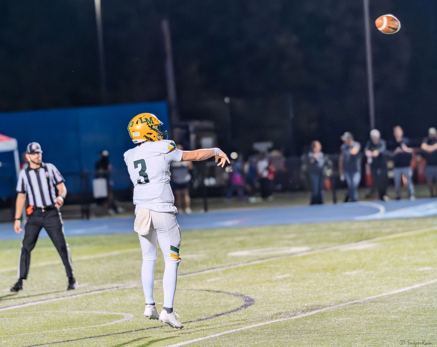 A football player wearing number 3 in gold and white uniform throws a pass during a night game.