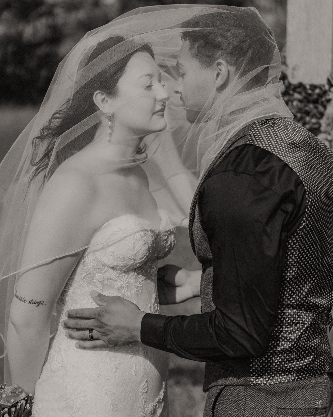 Black and white romantic photo of bride and groom sharing an intimate moment under a flowing wedding veil.