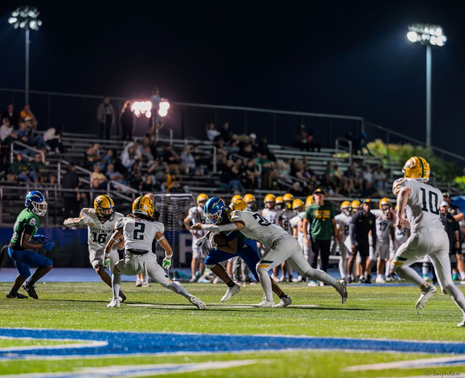 High school football players in white uniforms attempt to evade defenders during night game action.