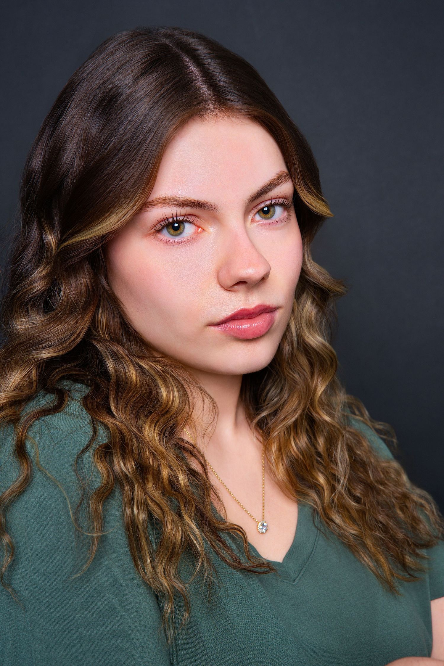 Young woman with wavy highlighted hair and pink eye makeup in green v-neck shirt.