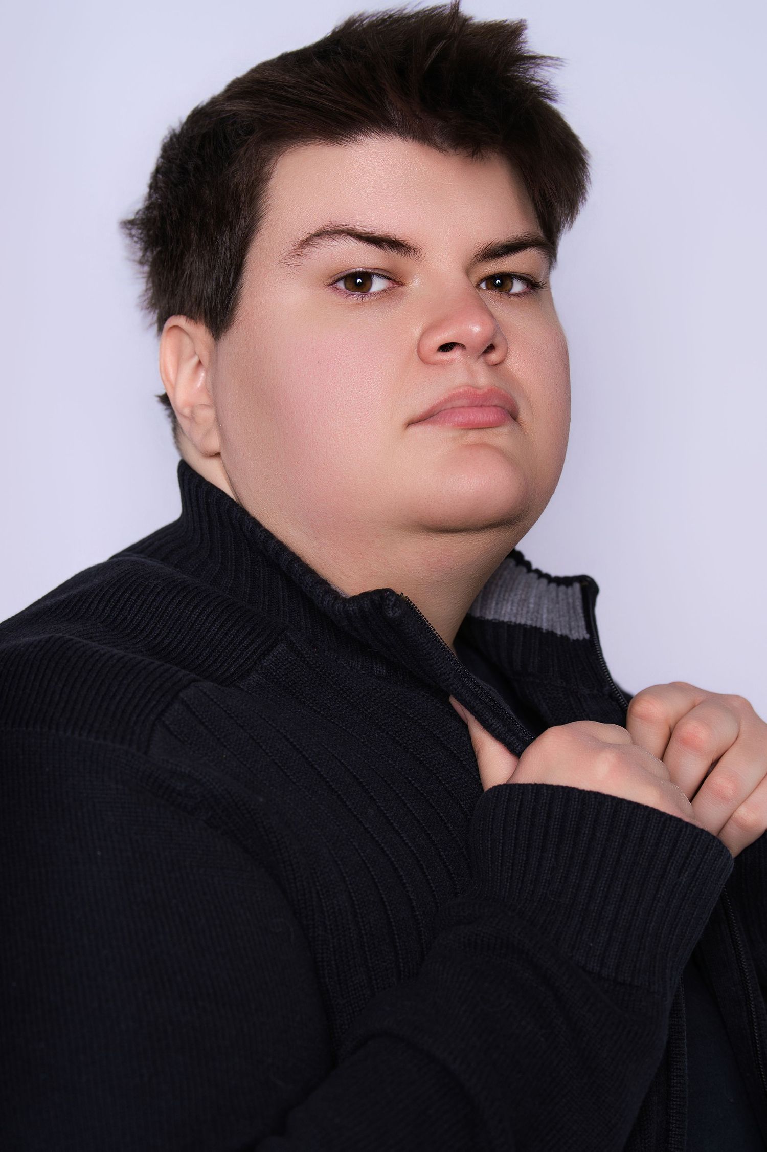 Young person with short dark hair wearing a black turtleneck sweater poses for a professional headshot against a light background.