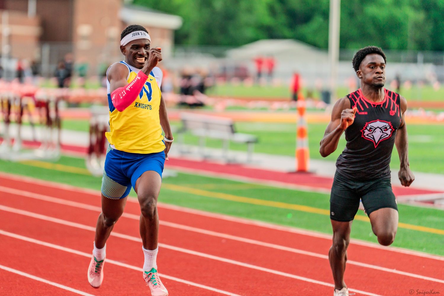 Two male sprinters compete in a close race on a red outdoor competition track.