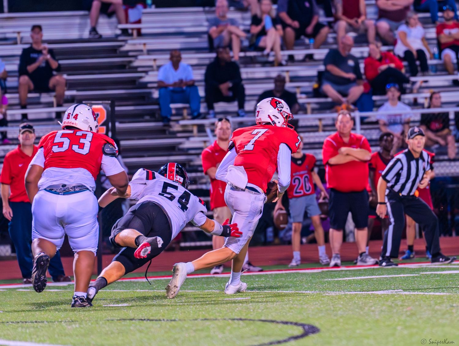 High school football players collide during tackle attempt in daytime game on turf field.