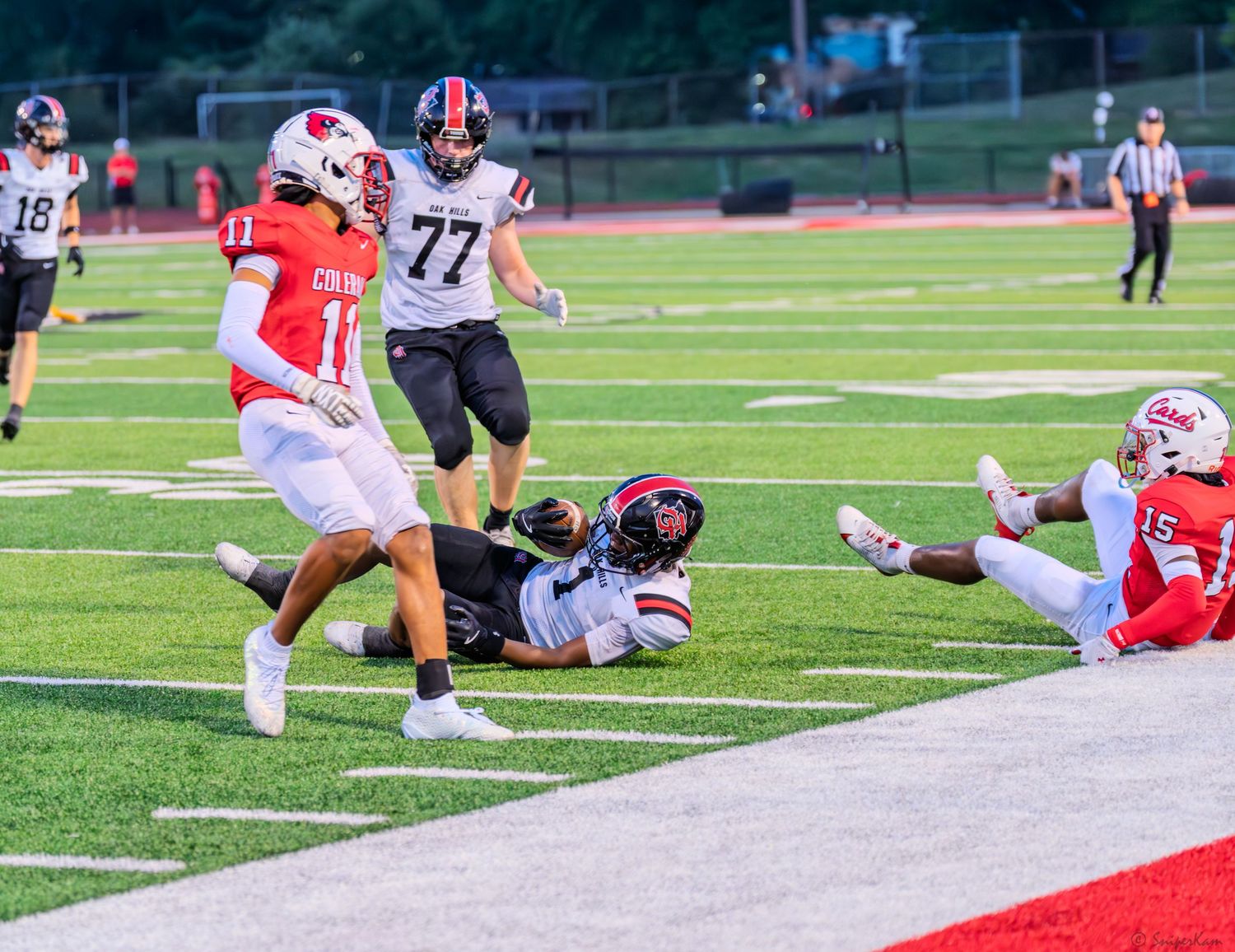 Football player dives for the end zone as defenders converge during a high school night game.