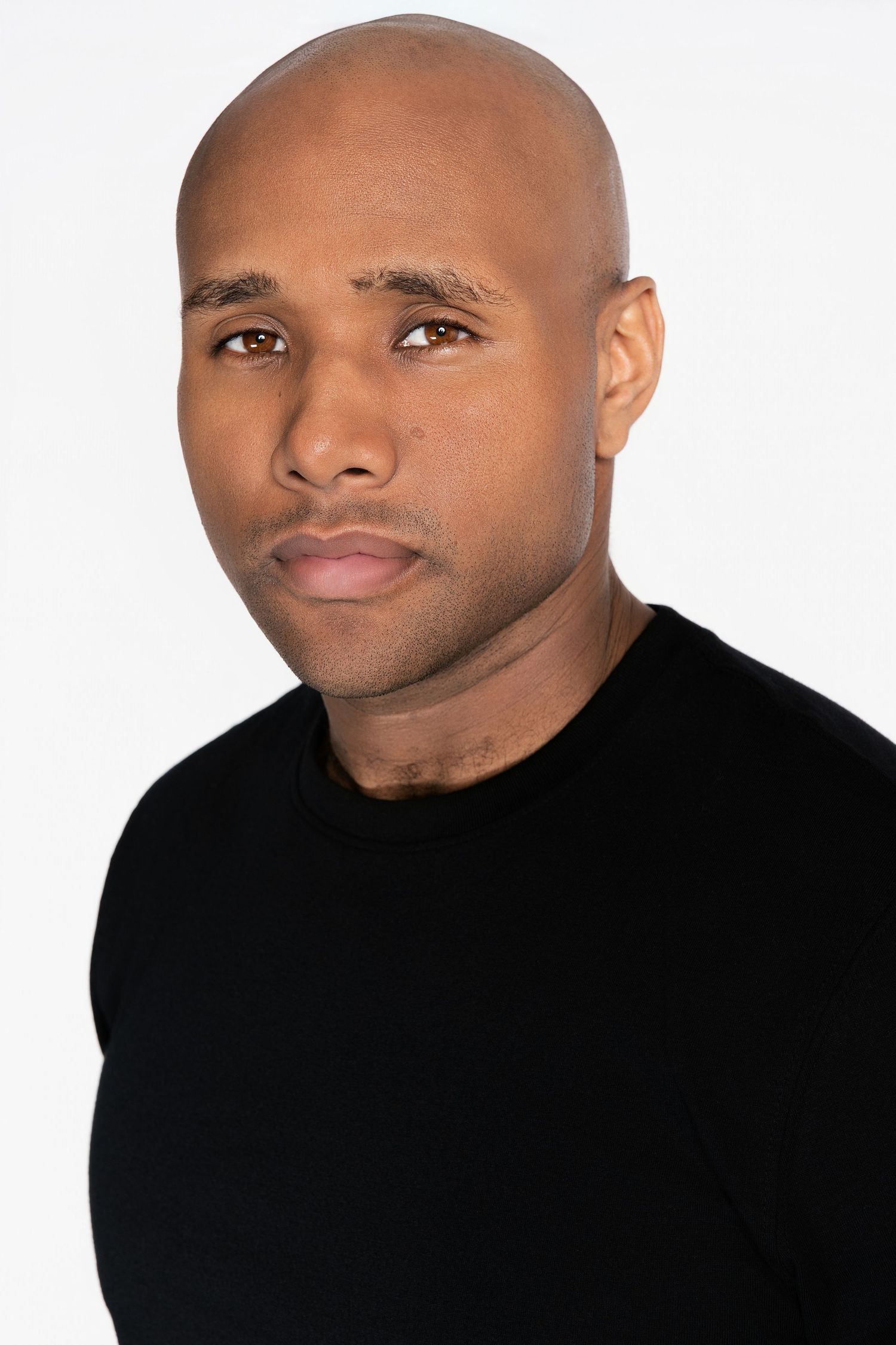 Bald man in black t-shirt with serious expression against white background.