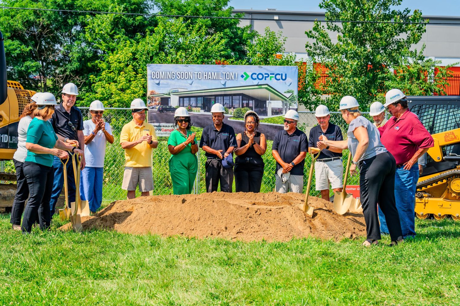 Diverse group of officials shoveling dirt at COPFCU credit union groundbreaking event in Hamilton.