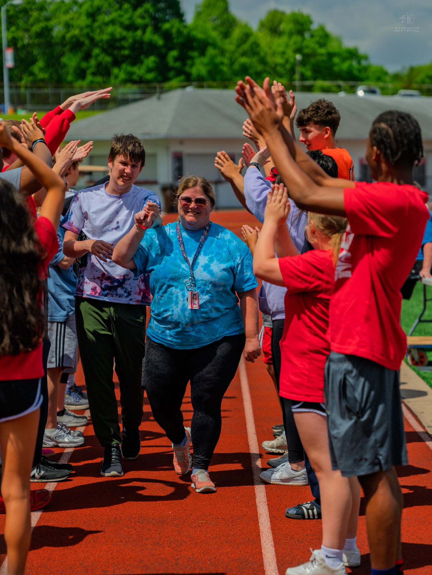 Teacher walks through high-five tunnel with students on outdoor track during school sports day celebration.