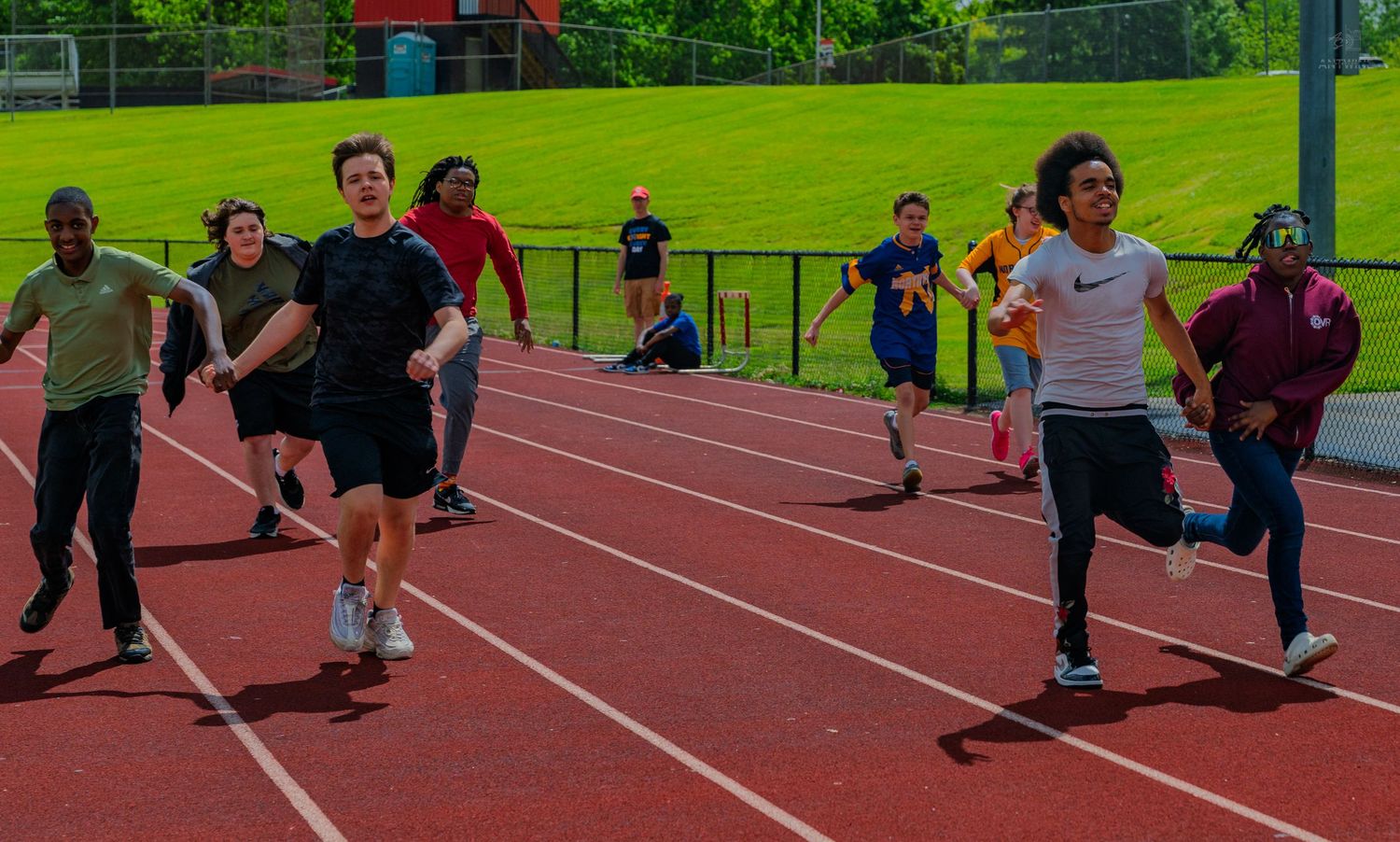 Students racing on a red outdoor track during a school track and field event on a sunny day.