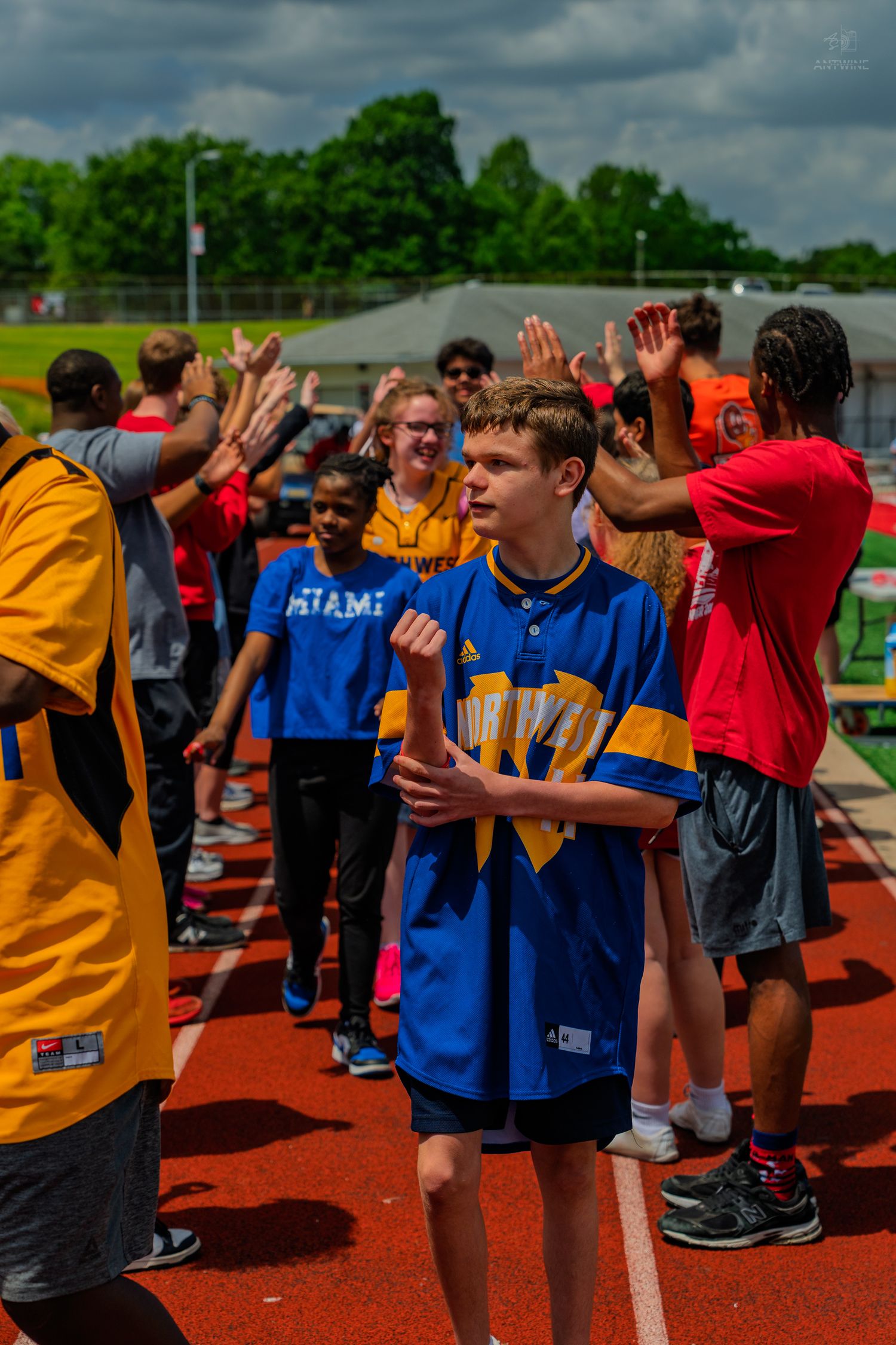 Students high-fiving on a red track during an outdoor school sports event on a cloudy day.