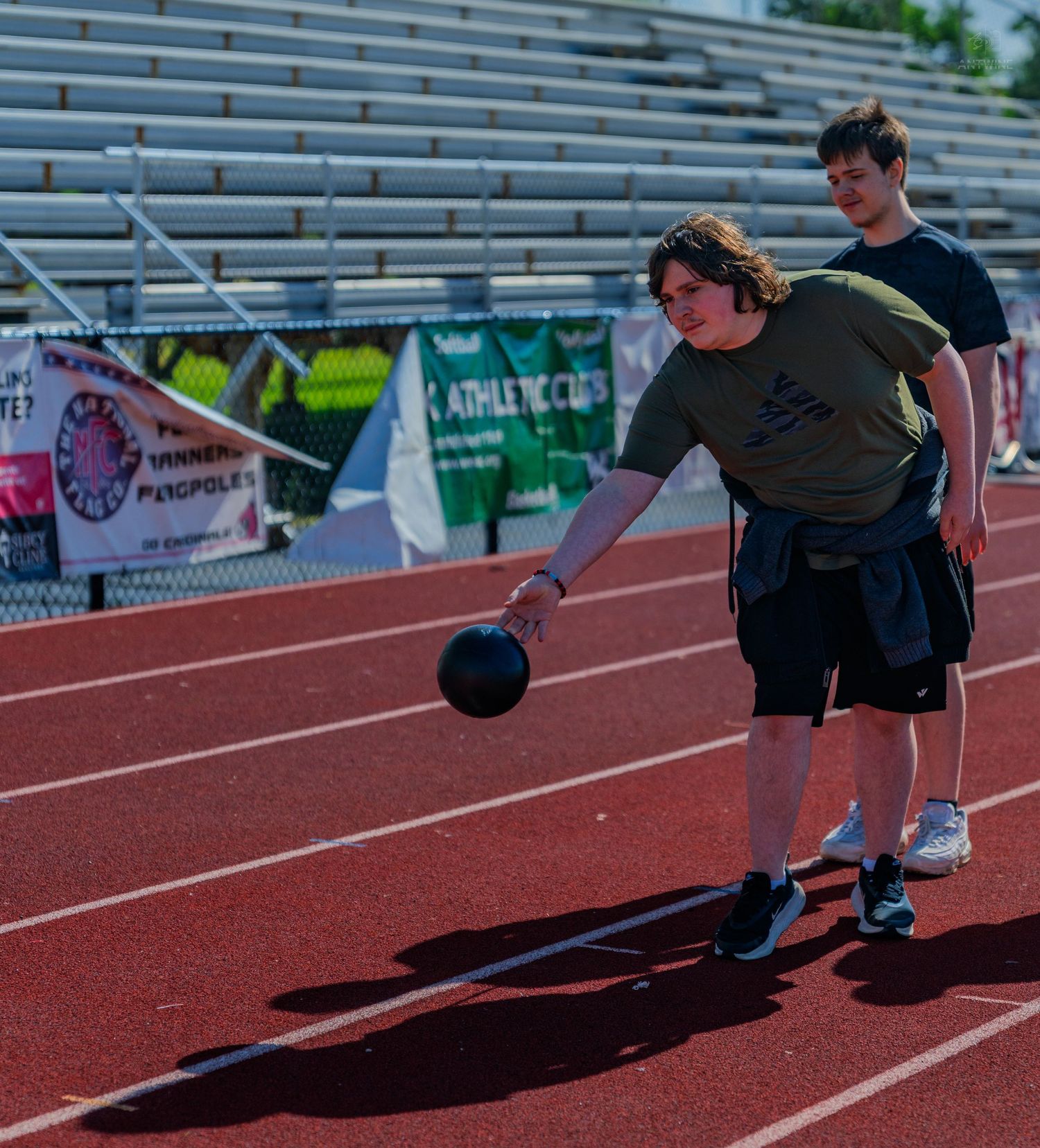 Athlete prepares to throw a shot put on a red track during an outdoor field event competition.