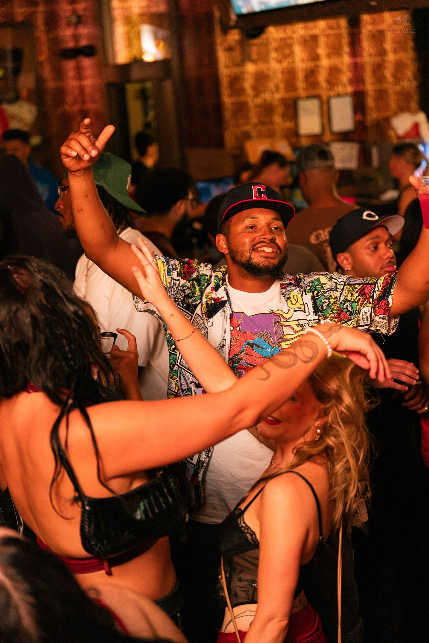 Man in colorful shirt and cap dancing energetically at a packed nightclub party.