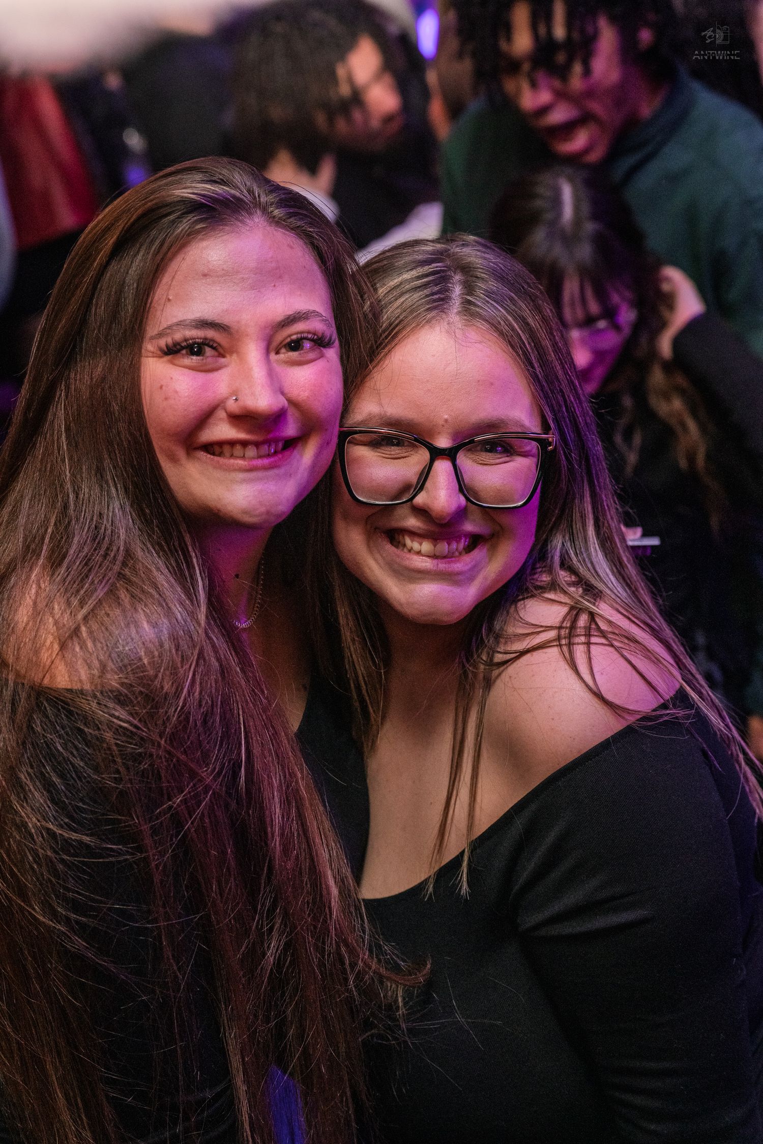 Two smiling women posing together under purple lights at a nightclub.