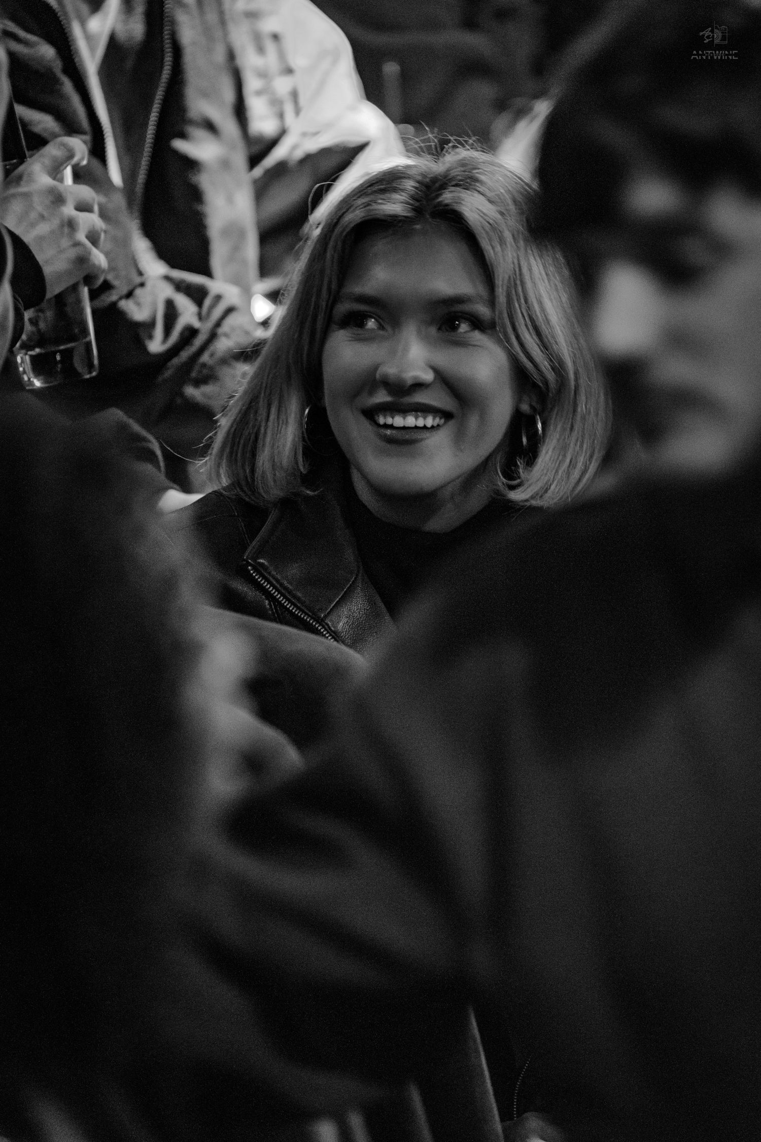 Black and white portrait of a smiling blonde woman with hoop earrings in a crowd.
