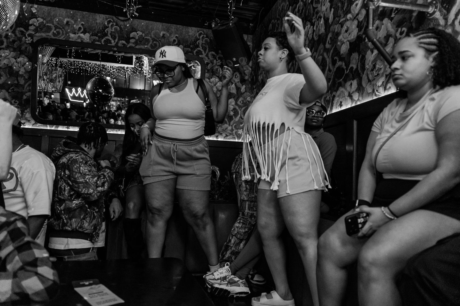 Women dancing and socializing at a bar wearing casual summer outfits, captured in black and white photography.