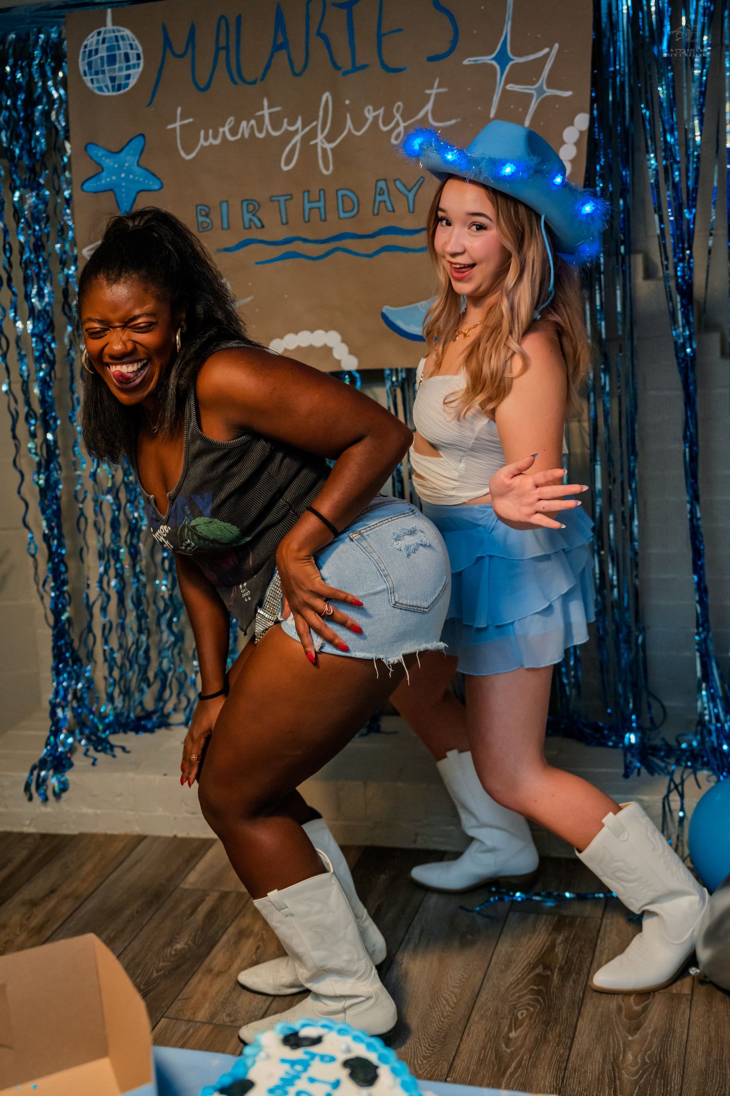 Two women laugh and dance together at Malarie's 21st birthday party near a decorated backdrop.