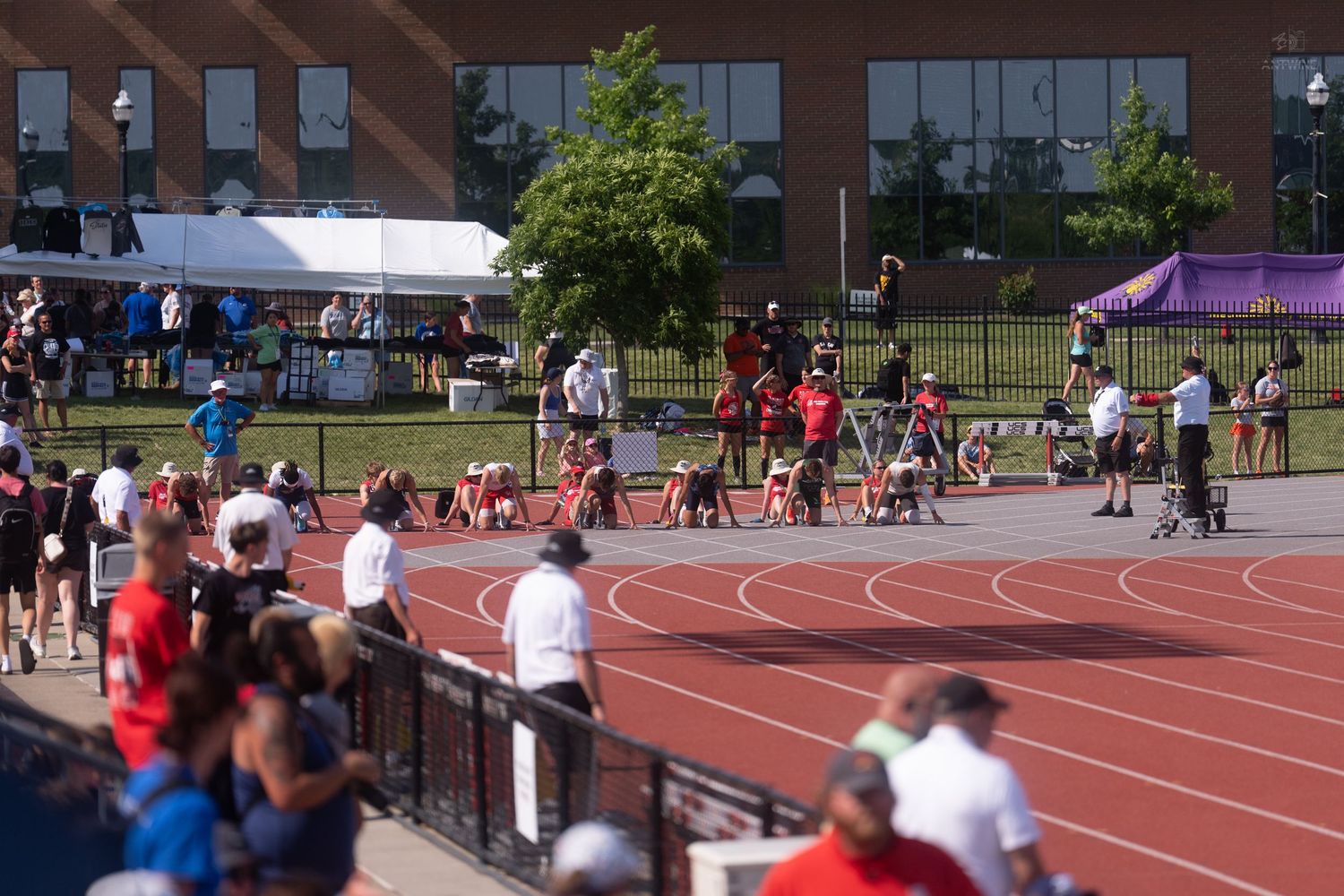Athletes prepare at the starting blocks while spectators watch at an outdoor track and field competition.