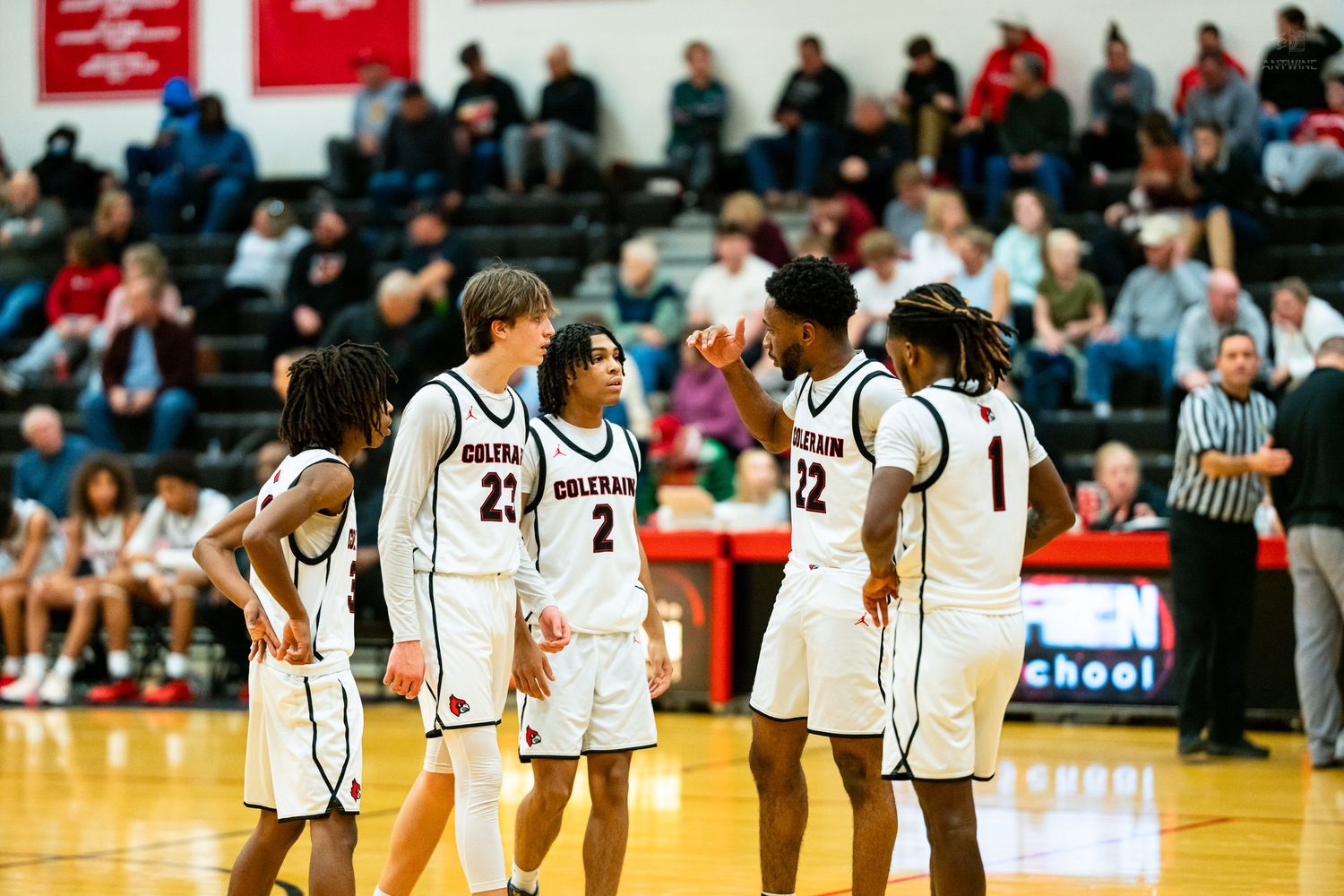 Five high school basketball players in white uniforms huddle together on the court during a game.