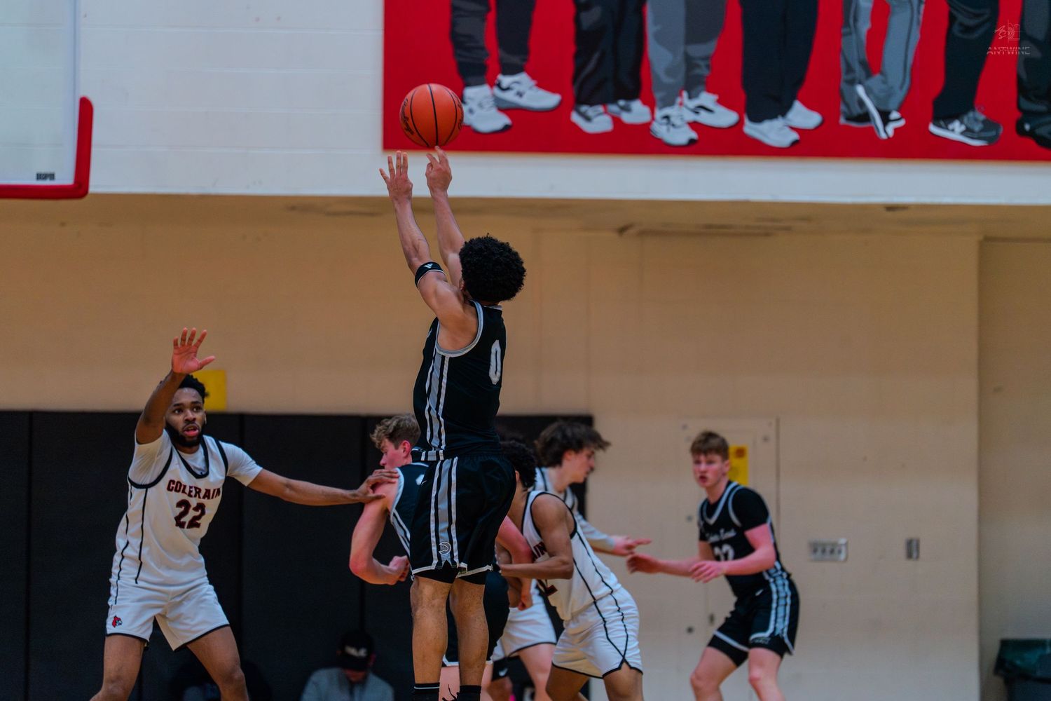 High school basketball player shoots a jump shot during a competitive indoor basketball game.