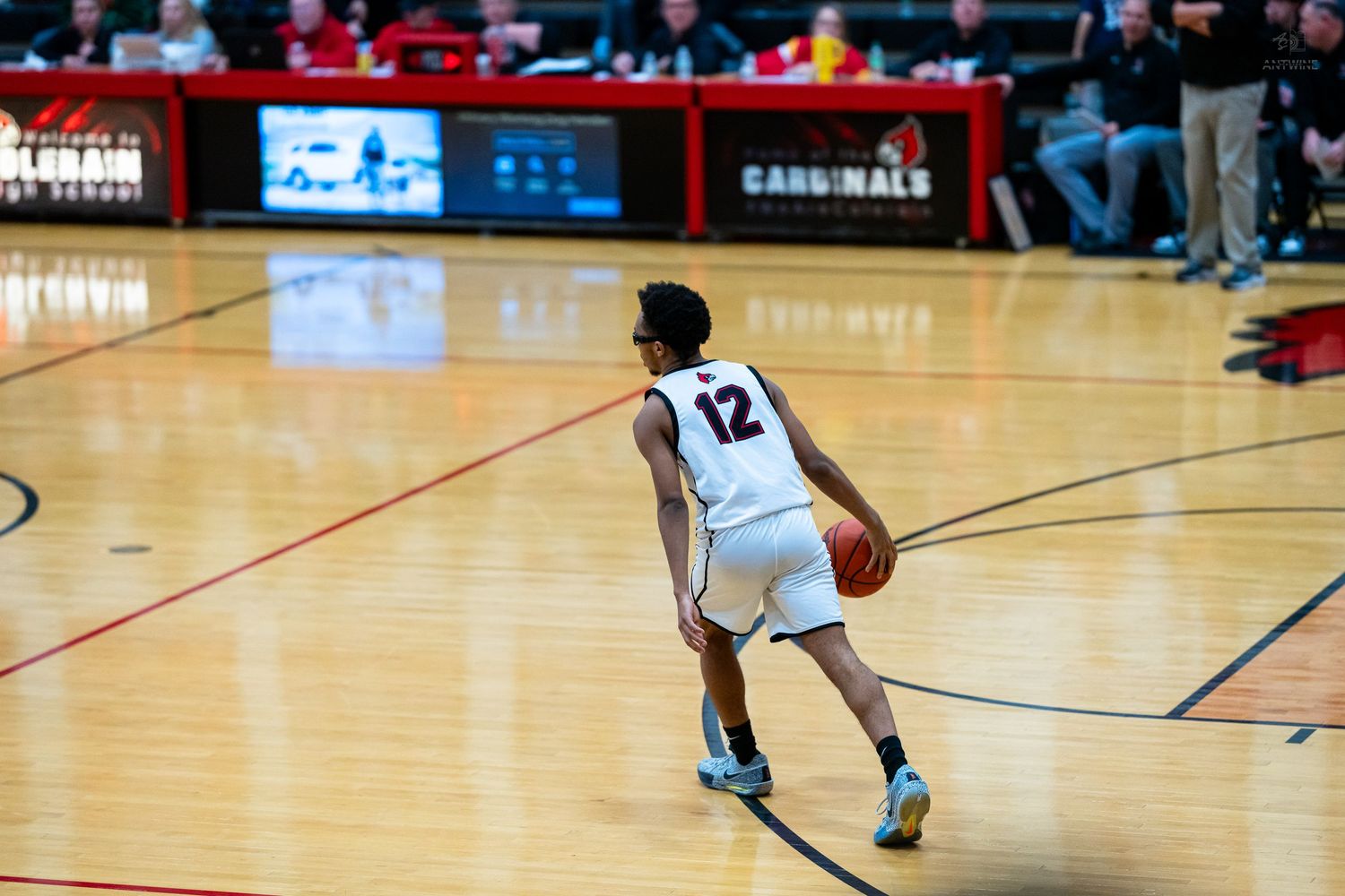 Player #12 dribbles basketball during high school Cardinals game on indoor court.
