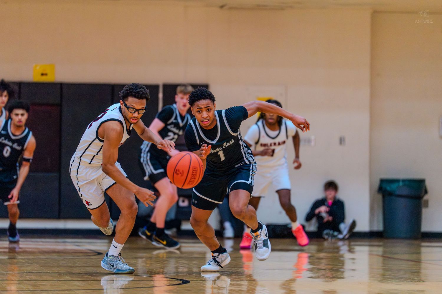 Basketball player drives past defender during an intense high school basketball game on a hardwood court.